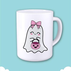 Op de afbeelding: Witte keramische mok met een cartoon spookontwerp. Het spook heeft een roze strik en houdt een roze pompoenemmer vast. De mok heeft een wit handvat en staat tegen een lichtblauwe achtergrond.