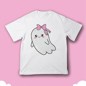 Op de afbeelding: Wit T-shirt met een cartoon spook met een roze strik. Het spook heeft een vriendelijke uitdrukking met roze wangen en grote ogen. Het ontwerp staat in het midden van het shirt, op een roze achtergrond.