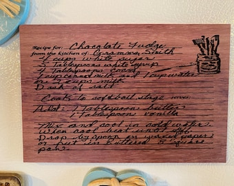 May include: A wooden recipe card with a handwritten recipe for Chocolate Fudge from Gramma Smith's kitchen. The recipe includes ingredients like white sugar, white syrup, cocoa, canned milk, and water. It also includes instructions to cook the fudge to a softball stage and add butter and vanilla.