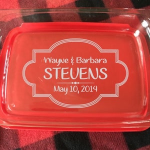 May include: A red glass baking dish with handles. The dish is personalized with the text "Wayne & Barbara STEVENS May 10, 2014" in a white script font.