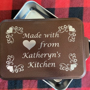 May include: Brown baking pan with a silver lid. The pan has a white inscription that reads "Made with love from Katheryn's Kitchen" with a heart design.