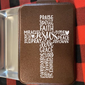 May include: A brown baking pan with a white cross design. The cross is made up of words like "Jesus", "Love", "Faith", "Grace", "Peace", and "Hope".