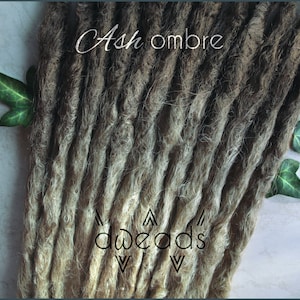 Peut inclure: Dreadlocks ombrés cendrés avec un dégradé de brun clair à brun foncé. Les dreadlocks sont faites de cheveux synthétiques et sont prêtes à être installées. Le texte "dreads" est visible en bas de l'image.