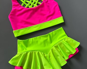 May include: A neon pink and green dance outfit with a criss-cross back on the top and a ruffled skirt.