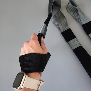 以下が含まれることがあります： 黒いリストストラップとクリーム色の文字盤の時計をつけた人が、黒とグレーのストラップをループ付きで持っています。