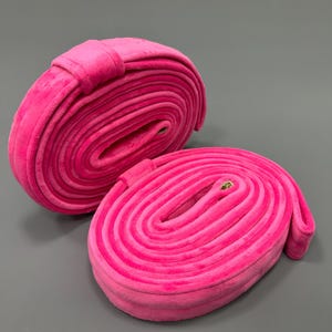 Peut inclure: Deux rouleaux de ruban en velours rose, chacun roulé en forme de cercle. Les rouleaux sont faits d'un tissu doux et pelucheux et ont un léger éclat.