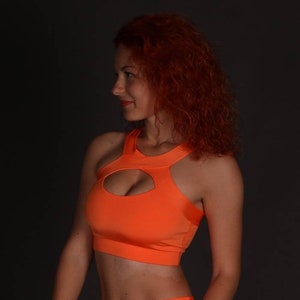 May include: A bright orange sports bra with a cut-out design in the front. The bra has a racerback style and is made of a stretchy, comfortable fabric.