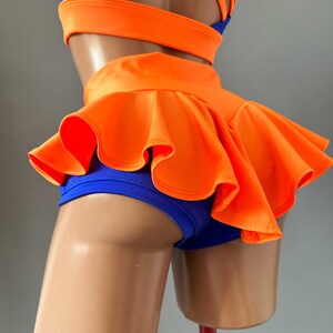 May include: A two-piece dance outfit in blue and orange. The top has a criss-cross strap design at the back. The bottom is a pair of shorts with a ruffled orange skirt overlay.