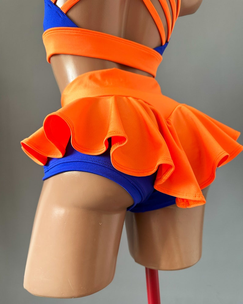 May include: A two-piece dance outfit in blue and orange. The top has a criss-cross strap design at the back. The bottom is a pair of shorts with a ruffled orange skirt overlay.
