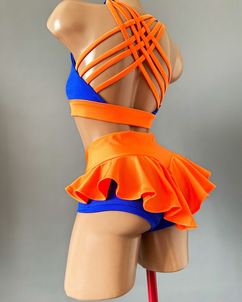 May include: A two-piece dance outfit in blue and orange. The top has a criss-cross back design and the bottom has a ruffled skirt.