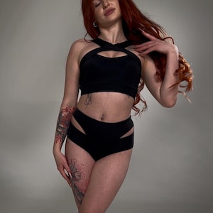 Pode incluir: Uma mulher vestindo um top preto curto e shorts de cintura alta com recortes. O top tem um design cruzado na frente. Os shorts têm cintura alta e recortes nas laterais. A mulher tem cabelo ruivo e está usando um brinco de argola de prata.