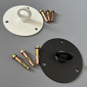 Op de afbeelding: Twee metalen plafondmontageplaten, één witte en één zwarte, elk met een bevestigde ooghaak. Drie goudkleurige bouten liggen naast elke plaat. De witte plaat heeft drie montagegaten.
