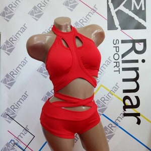 Op de afbeelding: Rode dansoutfit met een haltertop en short. De top heeft uitsnijdingen en gekruiste banden. De short heeft een hoge taille en uitsnijdingen aan de zijkanten.