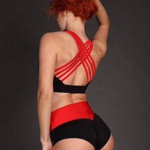 Puede incluir: Sujetador deportivo negro y rojo con tirantes cruzados en la espalda. Pantalones cortos de cintura alta a juego en negro y rojo con una cintura roja.