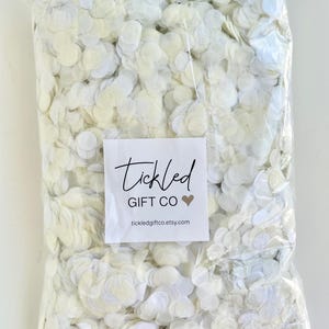 May include: A white plastic bag filled with white paper confetti circles. The bag has a label that says "Tickled Gift Co" with a heart and the website "tickledgiftco.etsy.com". The bag is labeled with "400g - approx. 50-60 guests".