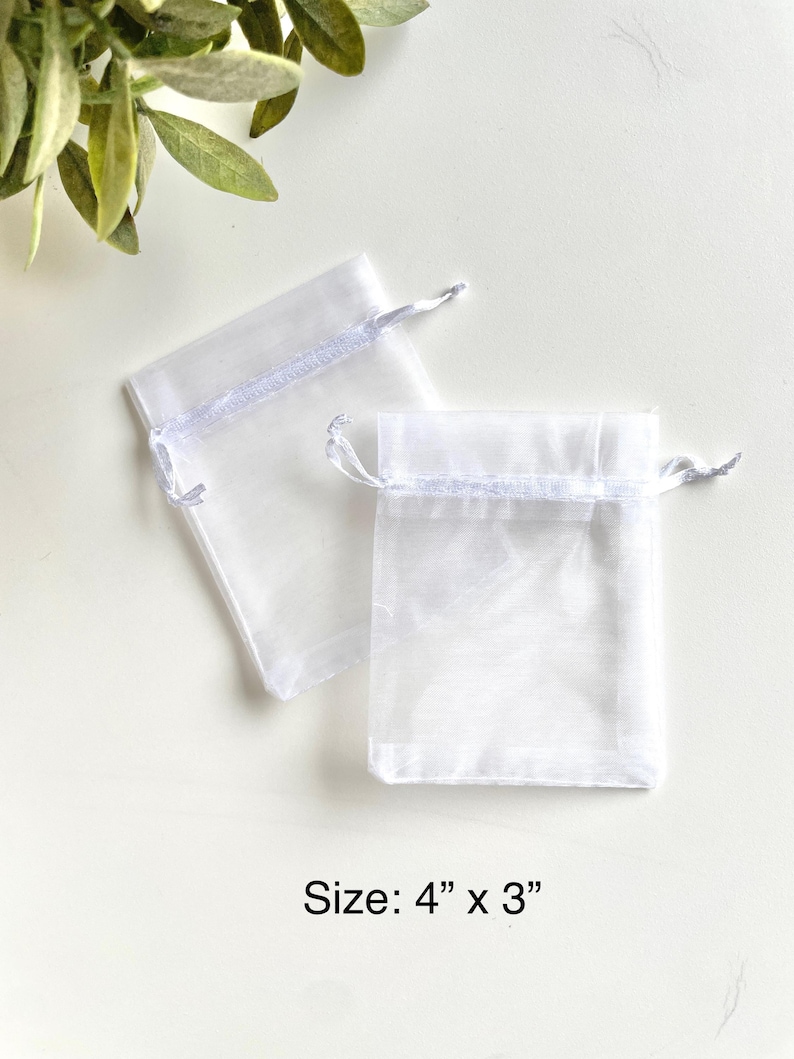 May include: Two white sheer organza gift bags with white ribbon ties. The bags are 4 inches by 3 inches.