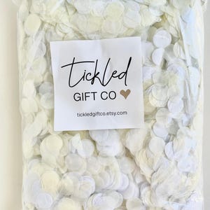 May include: A clear plastic bag filled with 180 grams of white confetti, enough for 25-30 guests. The bag has a label that says "Tickled Gift Co" and a website address.
