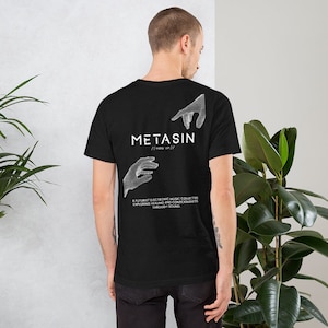 Może przedstawiać: Czarny T-shirt z białym tekstem, który brzmi "METASIN (mata sin)/ A FUTURIST ELECTRONIC MUSIC COLLECTIVE EXPLORING HEALING AND CONSCIOUSNESS THROUGH SOUND". Koszulka przedstawia dwie białe, stylizowane dłonie, które sięgają do siebie.