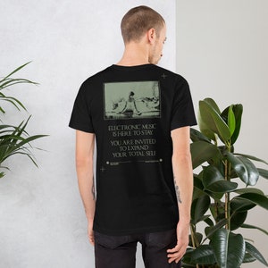 May include: Black t-shirt with a graphic print of a person sitting on a beach. The text on the shirt reads "Electronic Music is Here to Stay. You are Invited to Expand Your Total Self."