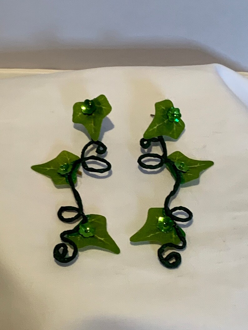May include: A pair of green leaf earrings with black wire vines and green glitter accents.
