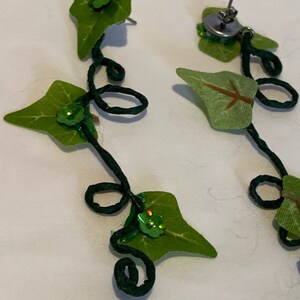 May include: A pair of green ivy leaf earrings with green sequins. The earrings are made with wire and fabric.