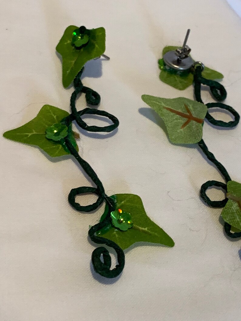 May include: A pair of green ivy leaf earrings with green sequins. The earrings are made with wire and fabric.