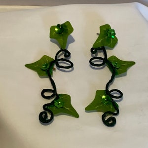 May include: A pair of green leaf earrings with black wire vines and green glitter accents.