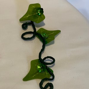 May include: A green ivy vine with three leaves and green glitter accents. The vine is made of wire and is curled into a decorative shape.