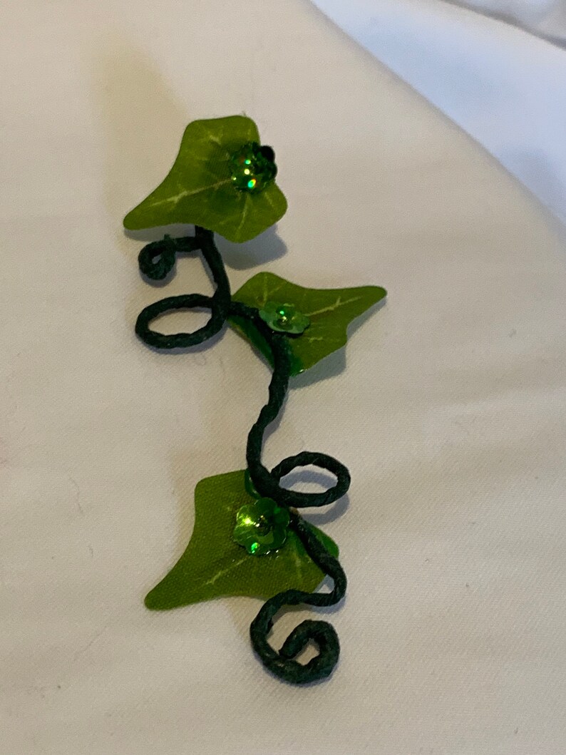 May include: A green ivy vine with three leaves and green glitter accents. The vine is made of wire and is curled into a decorative shape.