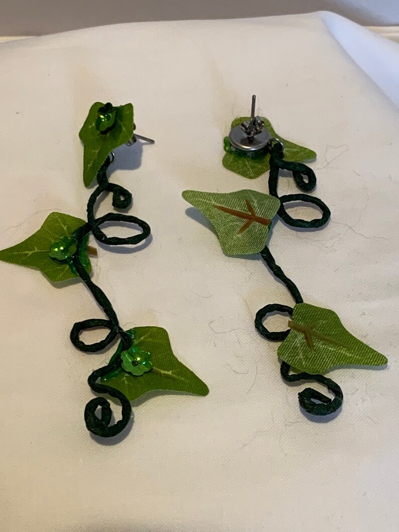 May include: A pair of green leaf earrings with a black wire vine design and green sequins. The earrings are dangling and have a silver post.