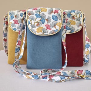 Peut inclure: Trois sacs bandoulière pour téléphone portable, de couleurs jaune, bleu et bordeaux. Chaque sac est doté d'un rabat orné d'un motif de feuilles bleues, jaunes et rouges sur fond blanc. Les sangles présentent également ce motif de feuilles.