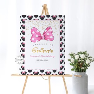 May include: A welcome sign for a second birthday party with a pink bow with white polka dots on a white background with black Minnie Mouse ears. The text on the sign reads "Welcome to Genevieve's Second Birthday May 2nd, 20XX".