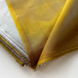 May include: A stack of fabric squares in shades of gold and white. The fabric has a soft, silky texture and a subtle sheen.