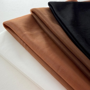 May include: A close-up of folded fabric in white, brown, and black. The fabrics have a sheer, mesh-like texture, with the brown fabric being the most prominent. The folds create shadows and depth, highlighting the different colours and textures.