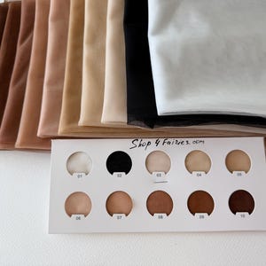 Puede incluir: Una selección de muestras de tela transparente en varios tonos de piel, que van desde el beige claro hasta el marrón oscuro. Una carta de colores con círculos numerados muestra los mismos tonos. El texto "Shop 4 Fairies.com" es visible.