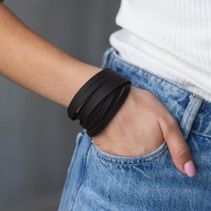 Puede incluir: Un brazalete de cuero negro con múltiples correas envueltas alrededor de la muñeca.