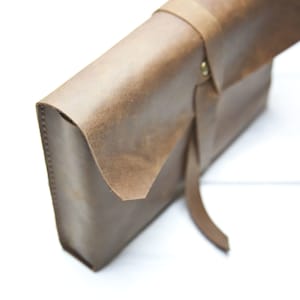 May include: A brown leather clutch with a flap closure and a long strap. The clutch is made of distressed leather and has a rustic look.