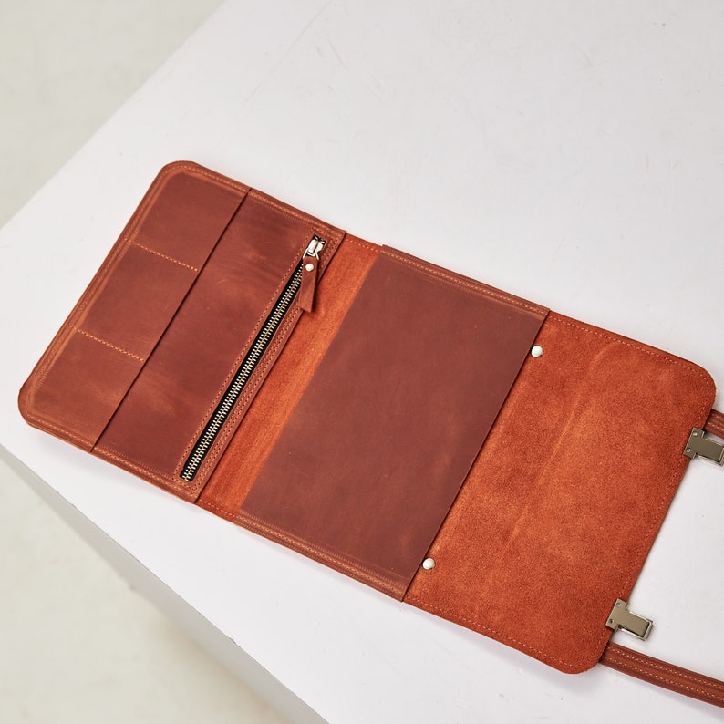 Op de afbeelding: Een bruine leren portfolio met een ritssluiting en een flap die met een drukknoop sluit. De portfolio is open om een leeg interieur te onthullen.