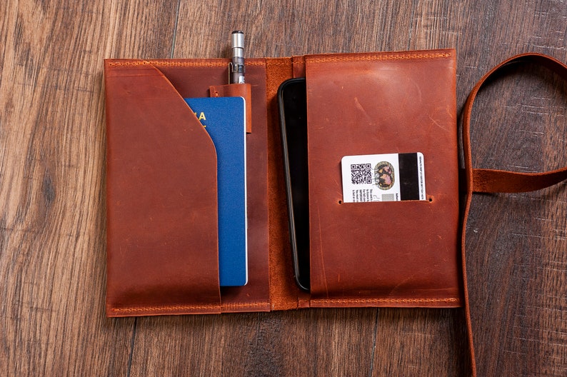 May include: A brown leather travel wallet with a passport, phone, and card holder. The wallet has a strap for carrying.