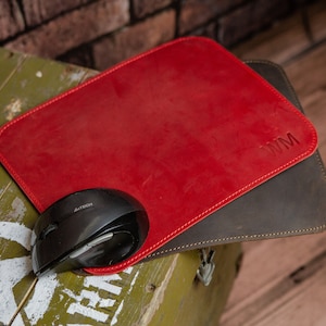 Könnte beinhalten: Ein rotes Leder-Mauspad mit den Initialen "WM" geprägt in der oberen rechten Ecke. Das Mauspad liegt auf einem braunen Leder-Mauspad. Eine schwarze Computermaus liegt auf dem roten Mauspad.