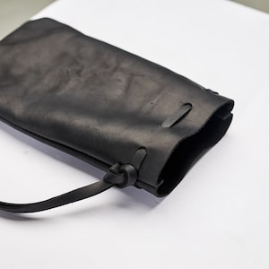 Pu&ograve; includere: Una borsa in pelle nera con una lunga tracolla. La borsa ha un design semplice ed &egrave; realizzata in pelle di alta qualit&agrave;.