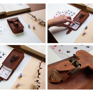 May include: A brown leather card case with a buckle closure. The case is open and a deck of playing cards is visible inside. There are also two dice on a white surface.