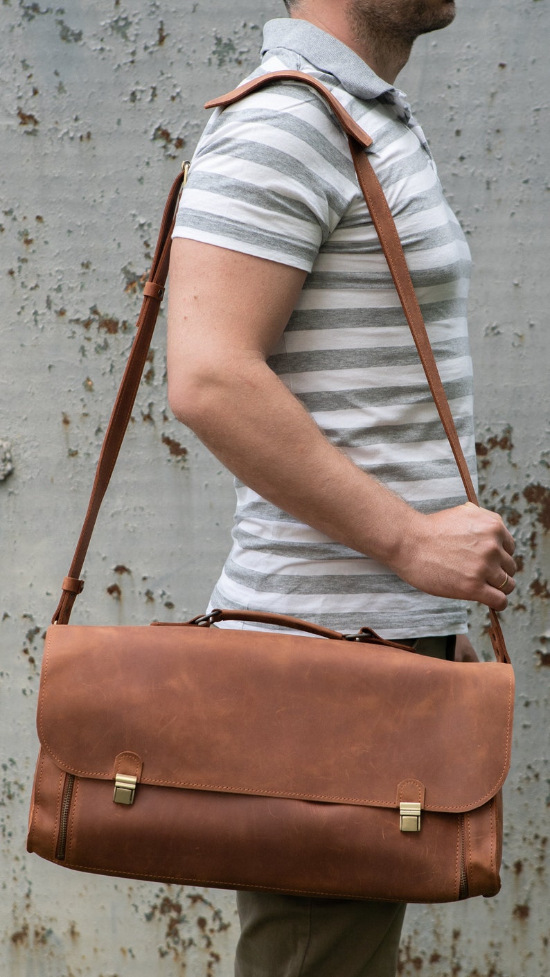 Pu&ograve; includere: Una borsa a tracolla in pelle marrone con una lunga tracolla regolabile. La borsa ha due fibbie metalliche e una cerniera sul davanti.