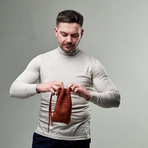 Pu&ograve; includere: Una persona che tiene una borsa di cuoio marrone con chiusura a coulisse.