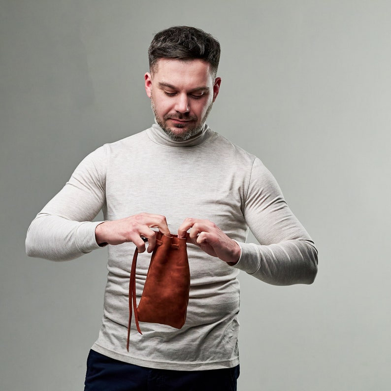 Pu&ograve; includere: Una persona che tiene una borsa di cuoio marrone con chiusura a coulisse.