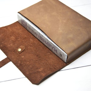 May include: A brown leather book cover with a strap and a snap closure. The cover is open to reveal a book titled "НИНДЖУ И ПРОКЛЯТИЯ".