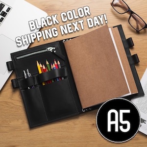 May include: Black leather A5 notebook with a zipper closure and multiple pockets for pens and pencils. The notebook has a brown paper insert and is open to reveal the blank pages.