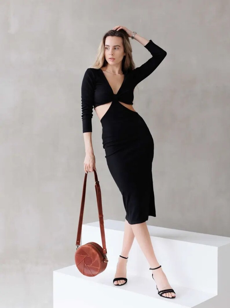 May include: A woman wearing a black midi dress with a cut-out detail and a brown leather circle bag with a strap.