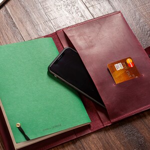 May include: A burgundy leather journal with a green notebook inside. The journal has a pocket on the outside that holds a credit card and a smartphone. The journal also has a strap and a pen.