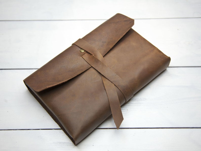May include: A brown leather envelope with a strap closure. The envelope is tied with a brown leather strap and has a brass button.